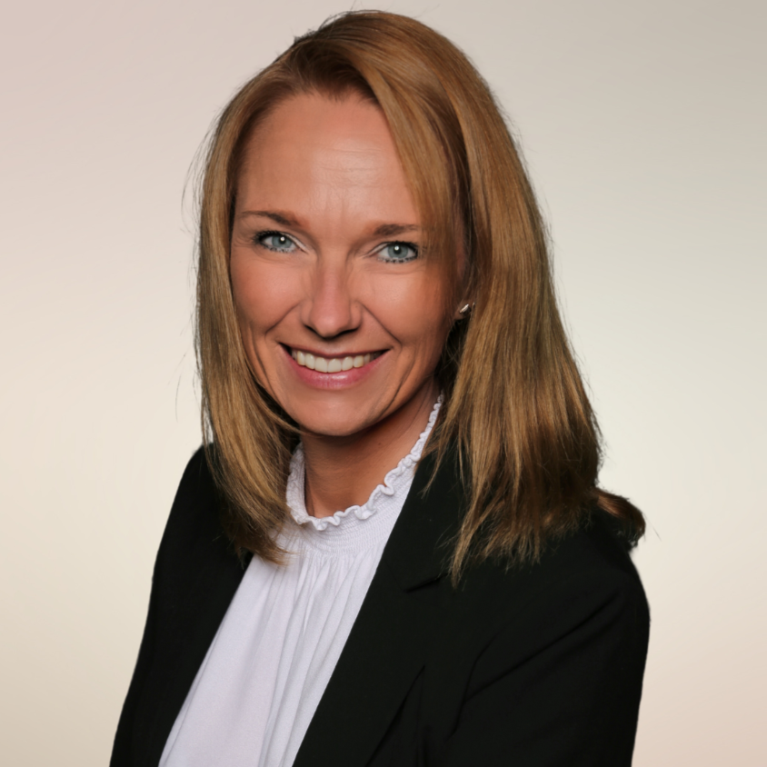 „Porträt einer lächelnden Frau im Business-Outfit vor neutralem Hintergrund – ideal zur Darstellung eines Teammitglieds oder einer Ansprechpartnerin.“